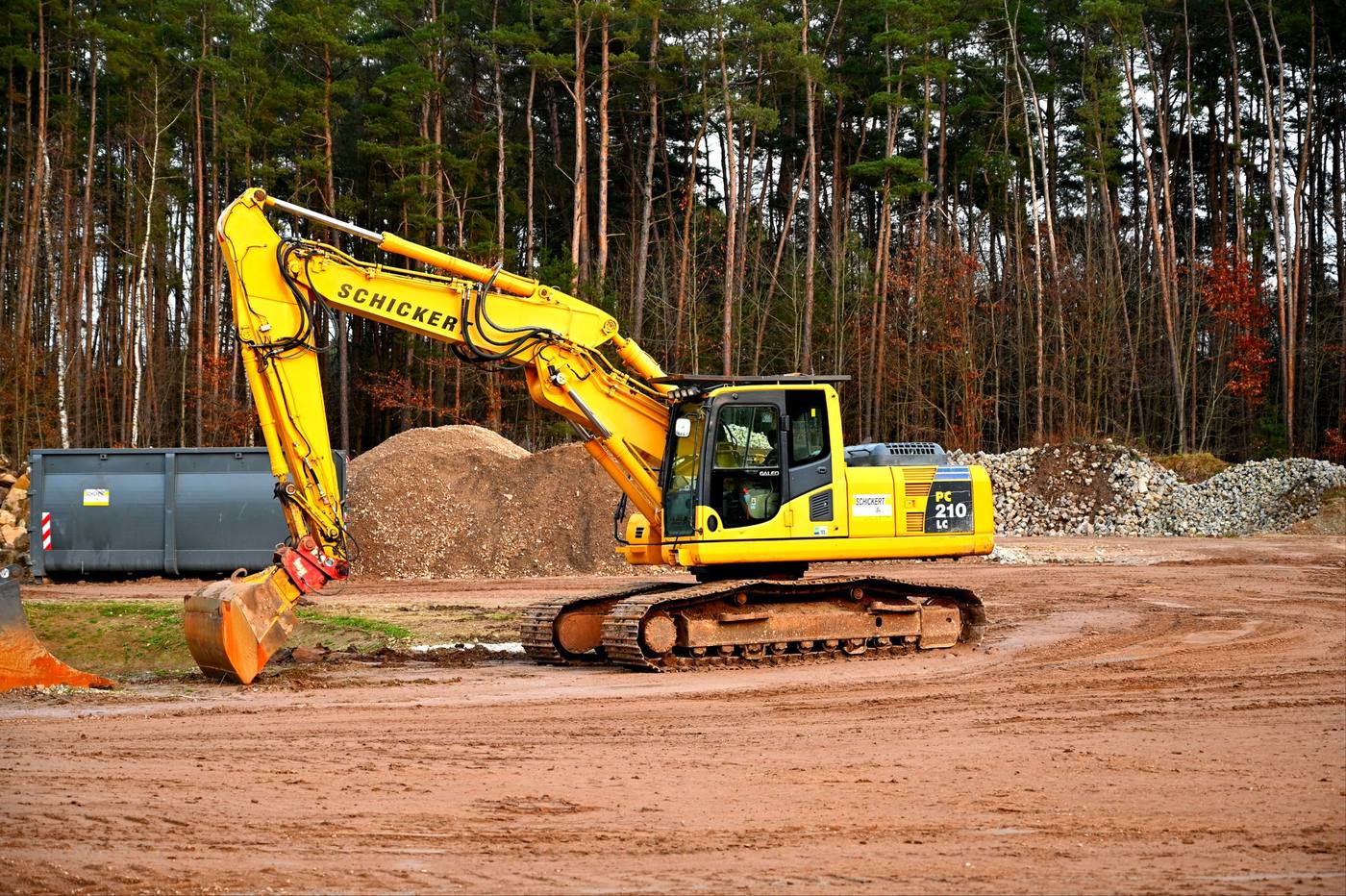 Kuvituskuva: tela-alustainen kaivinkone ja maakasa mäntymetsän reunassa.