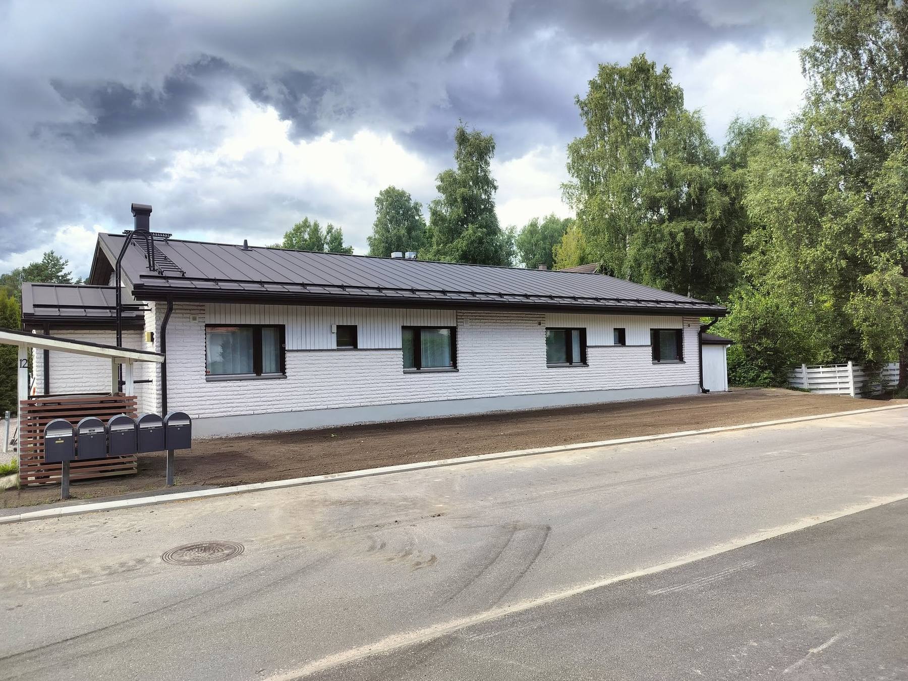 Valmis piha-alue tien varressa: valkoinen tiilitalo, tumma peltikatto ja tasattu, täytetty piha.